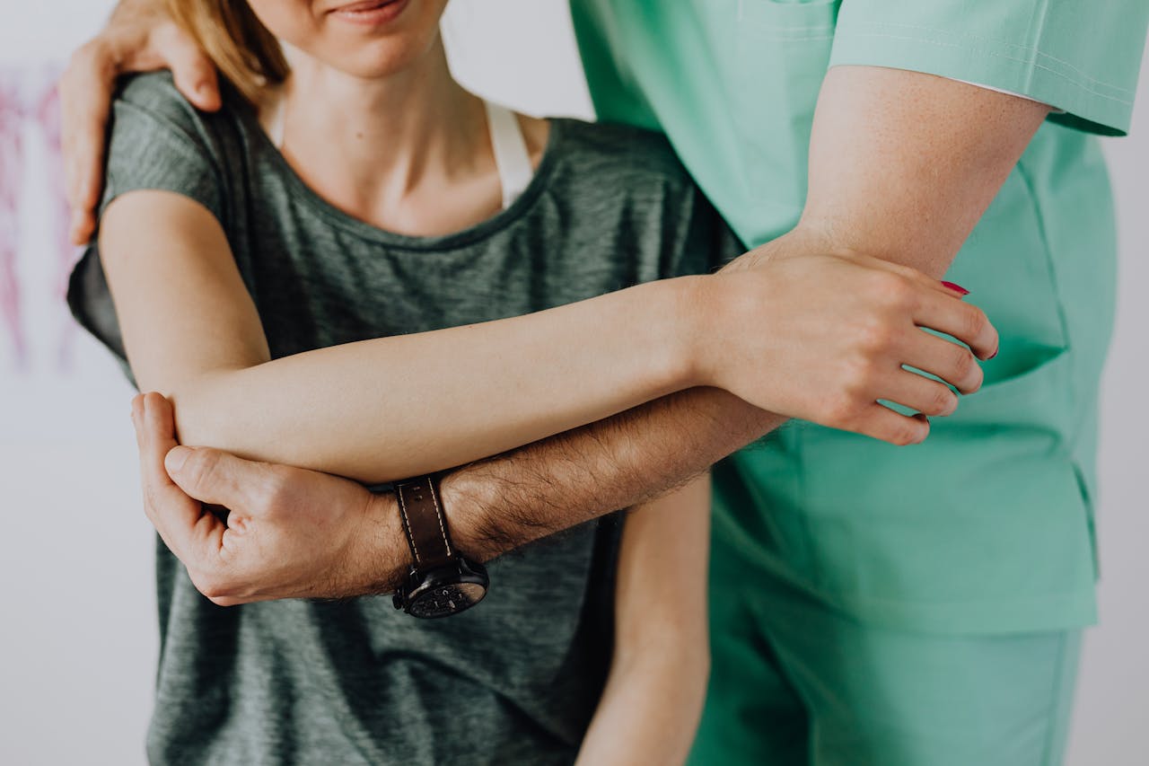 Crop unrecognizable orthopedist stretching shoulder of female patient